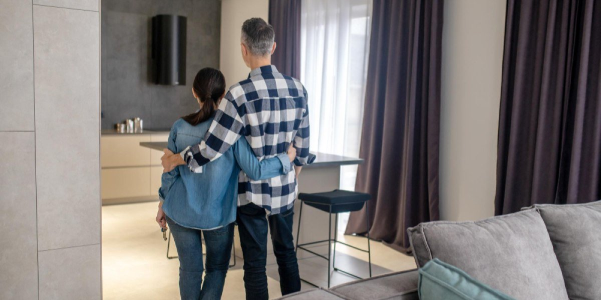 visão de um homem e uma mulher de costas abraçados, de pé na sala de um apartamento pequeno segurando as chaves da casa.