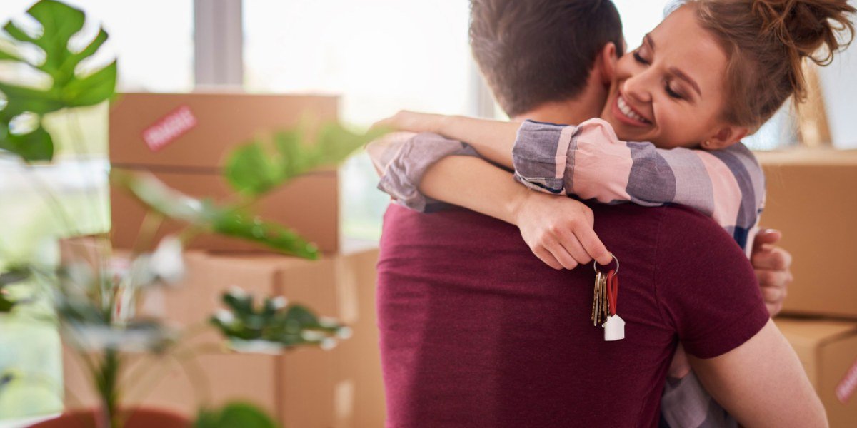 casal hétero se abraça em comemoração à mudança para sua casa própria enquanto a mulher segura as chaves da propriedade.