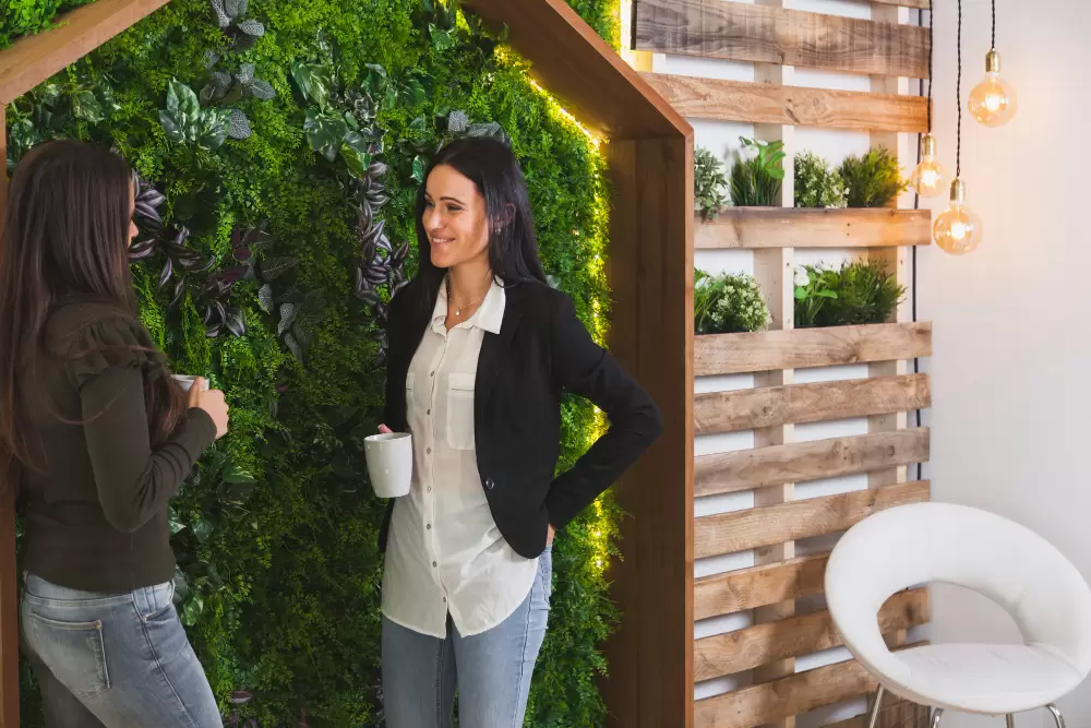 duas mulheres tomam café e conversam de pé em frente a um jardim vertical interno