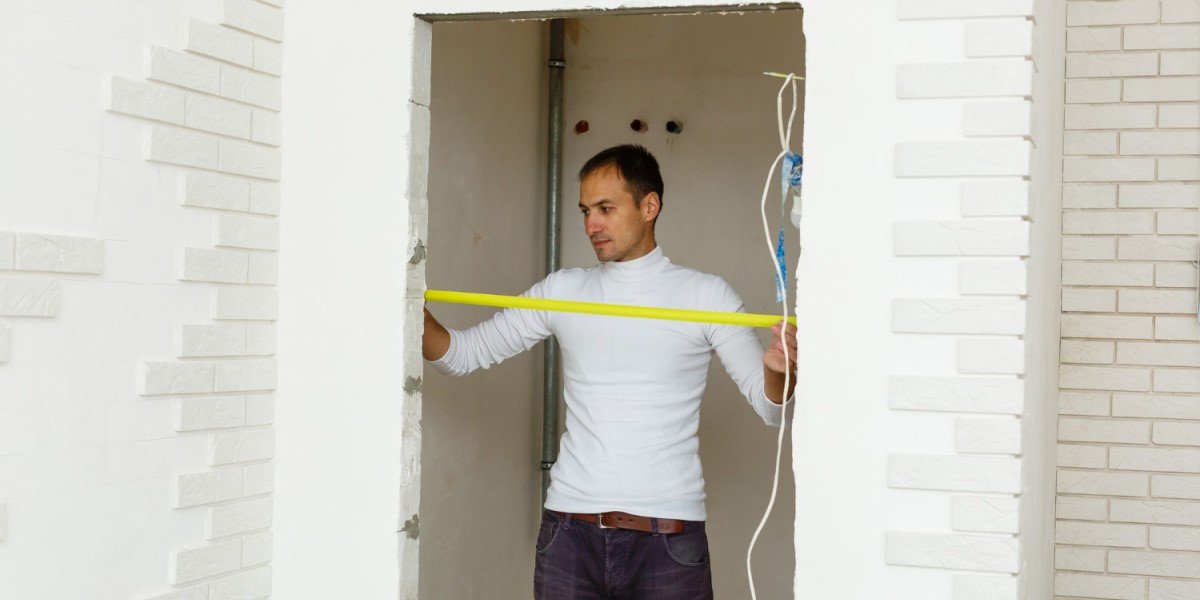 Homem jovem de camiseta branca medindo a largura de uma porta com uma fita métrica amarela