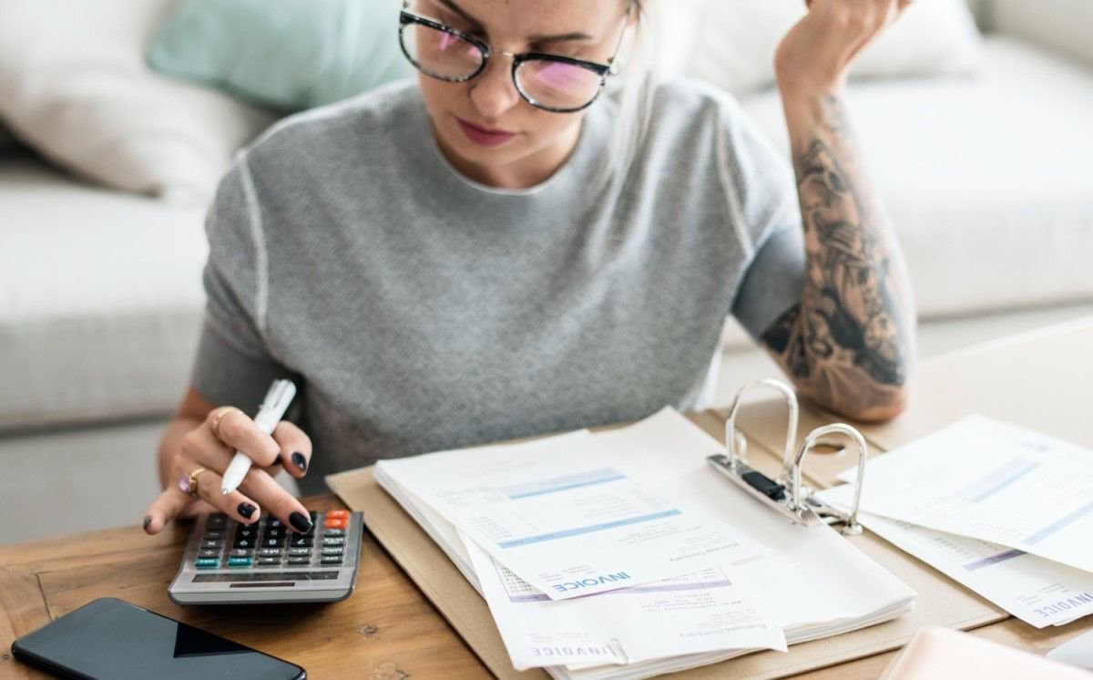 Mulher usando óculos e calculadora enquanto faz anotações em documentos financeiros