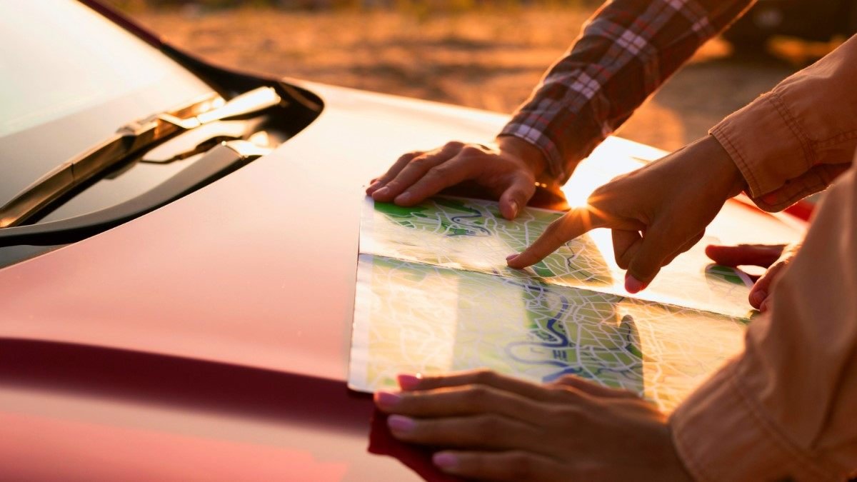 Duas pessoas examinando um mapa de papel sobre o capô de um carro vermelho ao entardecer. 