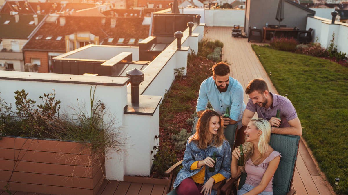 Amigos conversando e rindo em um terraço ao entardecer.