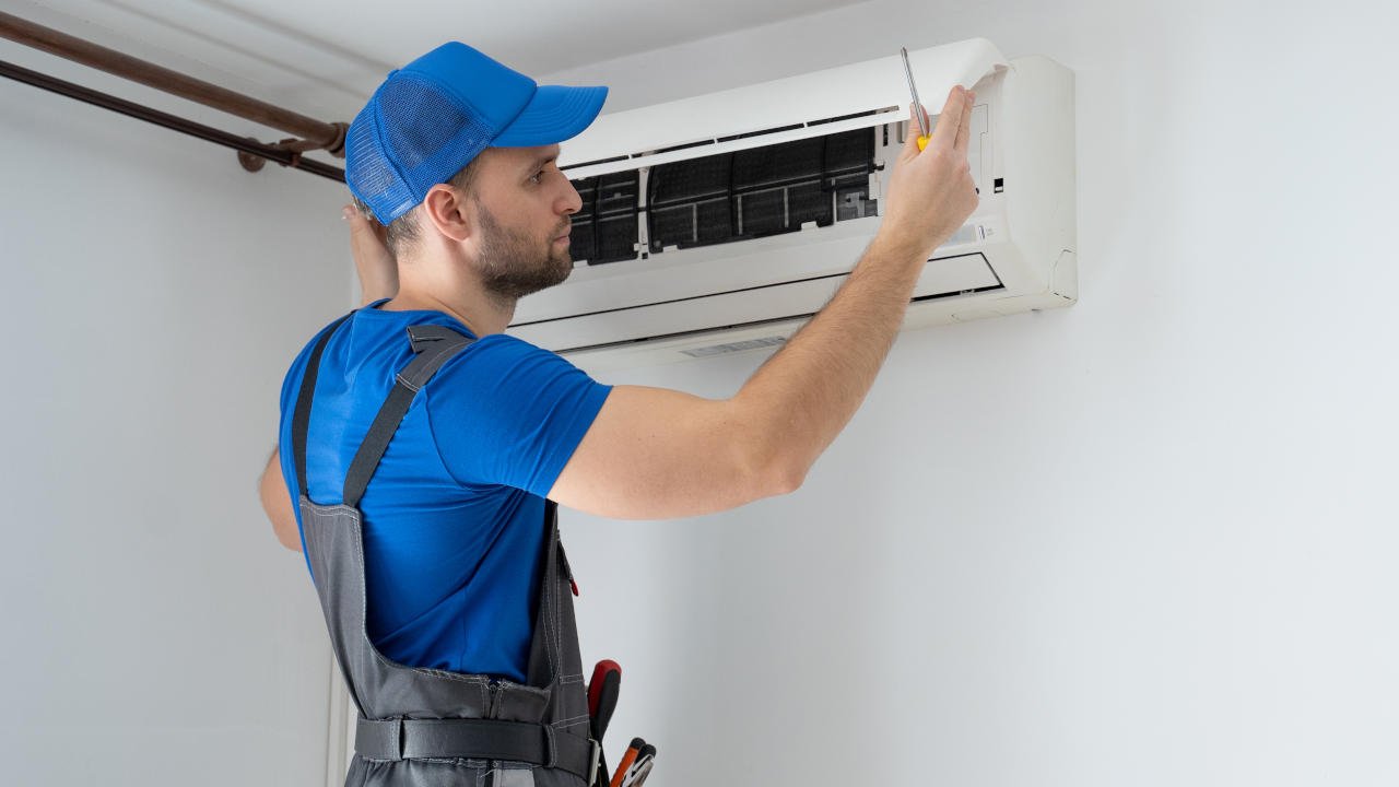 Técnico realizando manutenção em uma unidade de ar-condicionado instalada na parede.