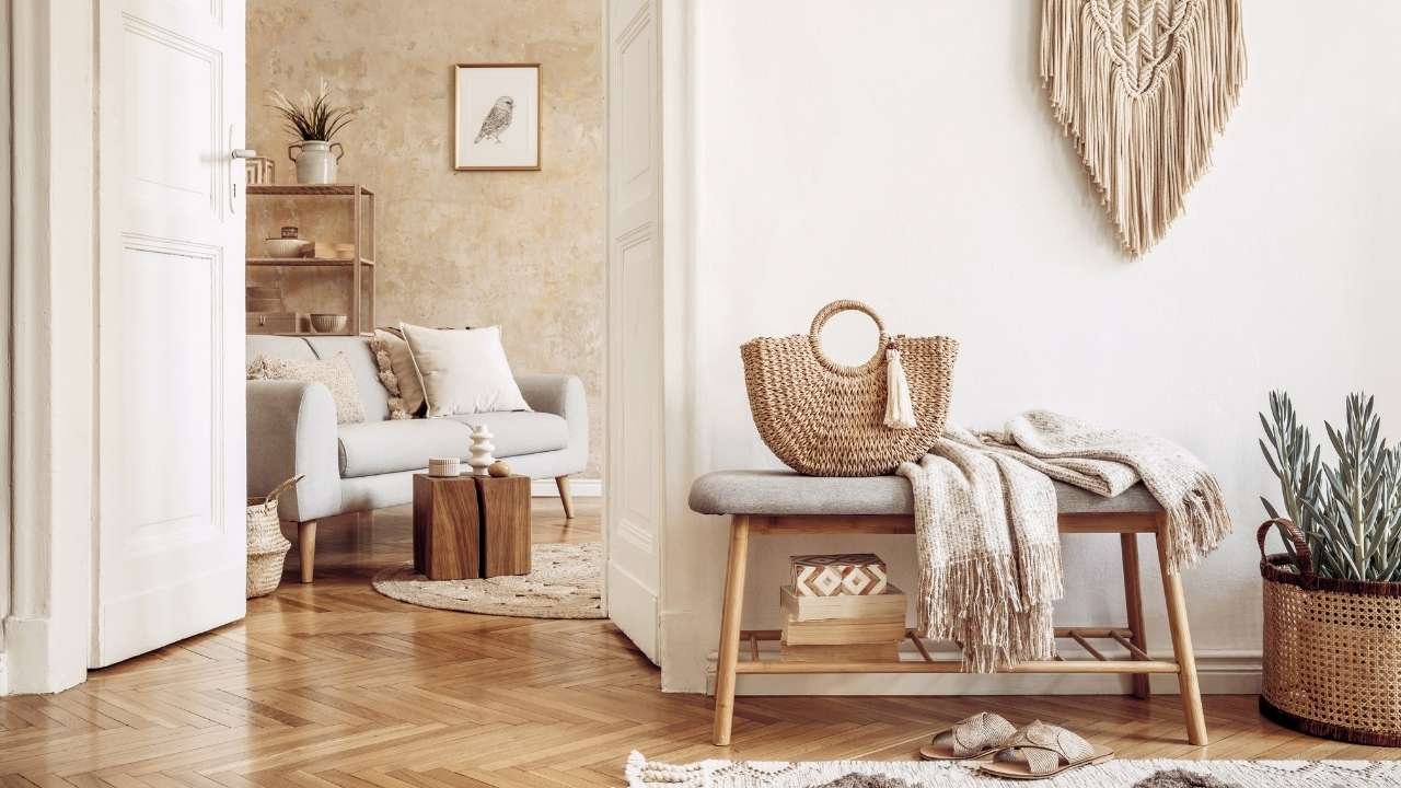 Hall de entrada com decoração boho, incluindo banco de madeira, cestas de palha e manta em tons naturais, com sala de estar ao fundo em um design harmonioso e leve.