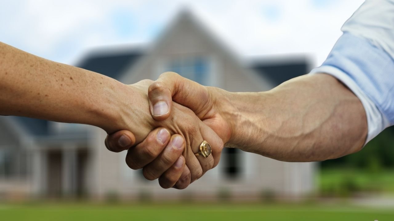 Aperto de mãos em frente a uma casa, simbolizando o fechamento de um negócio ou acordo relacionado a imóveis.