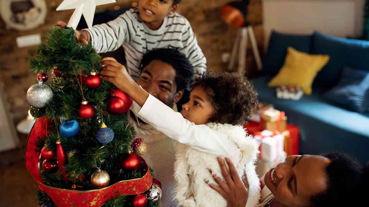 Família decorando uma árvore de Natal com enfeites coloridos em um ambiente aconchegante.