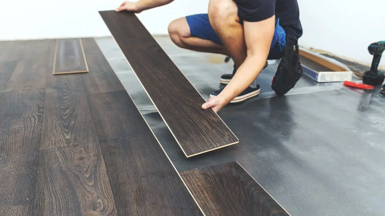 Pessoa instalando piso laminado escuro em um ambiente interno.