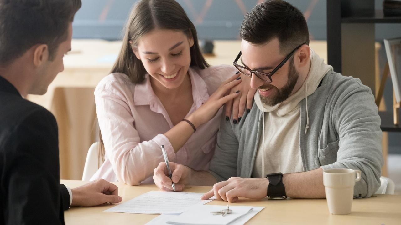 Casal assinando contrato com um corretor ao lado.