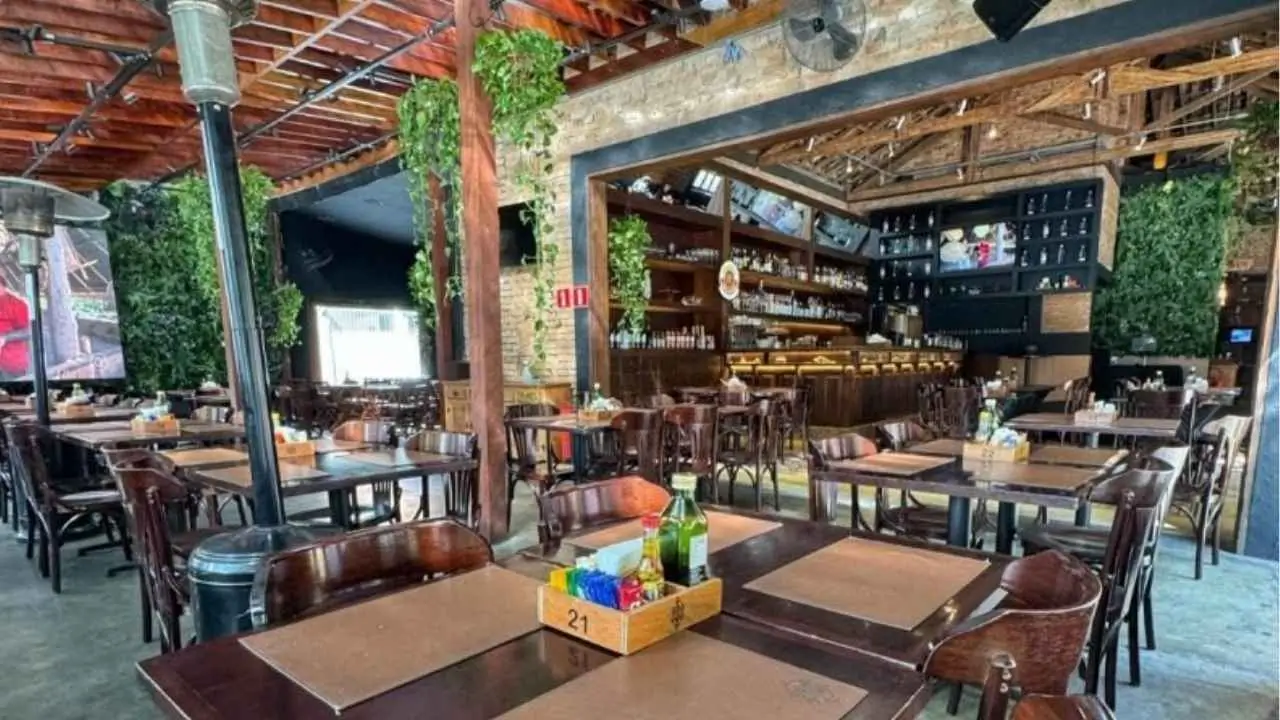 Interior de um restaurante com mesas e cadeiras de madeira, decorado com plantas.