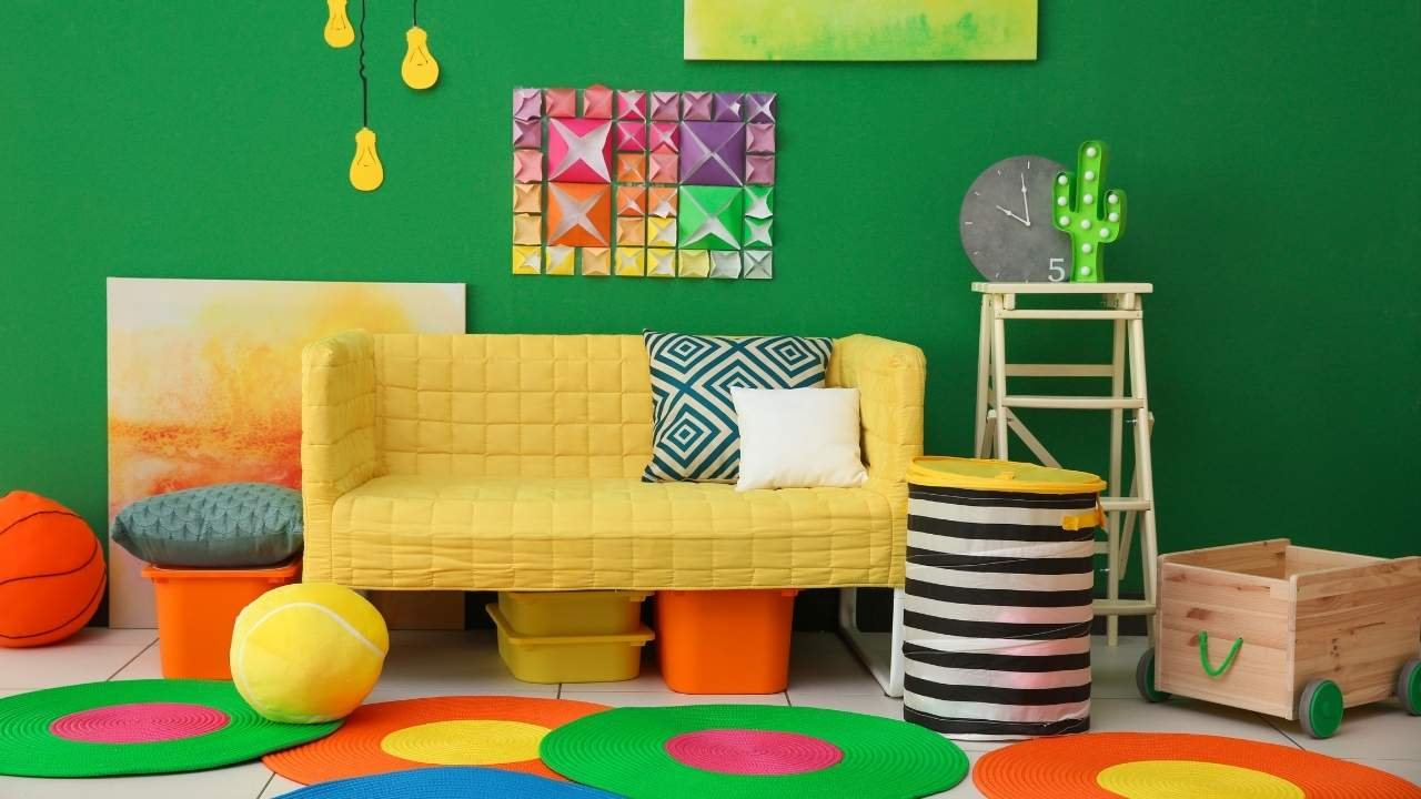 Ambiente decorado de forma colorida com sofá amarelo, almofadas geométricas, puffs coloridos, detalhes verdes, e decoração moderna na parede.