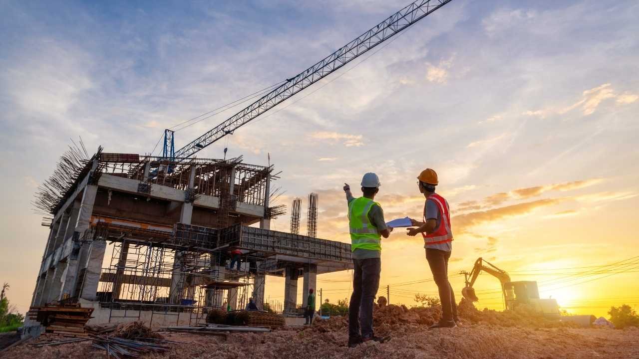 Obra em andamento com operários e grua ao entardecer.
