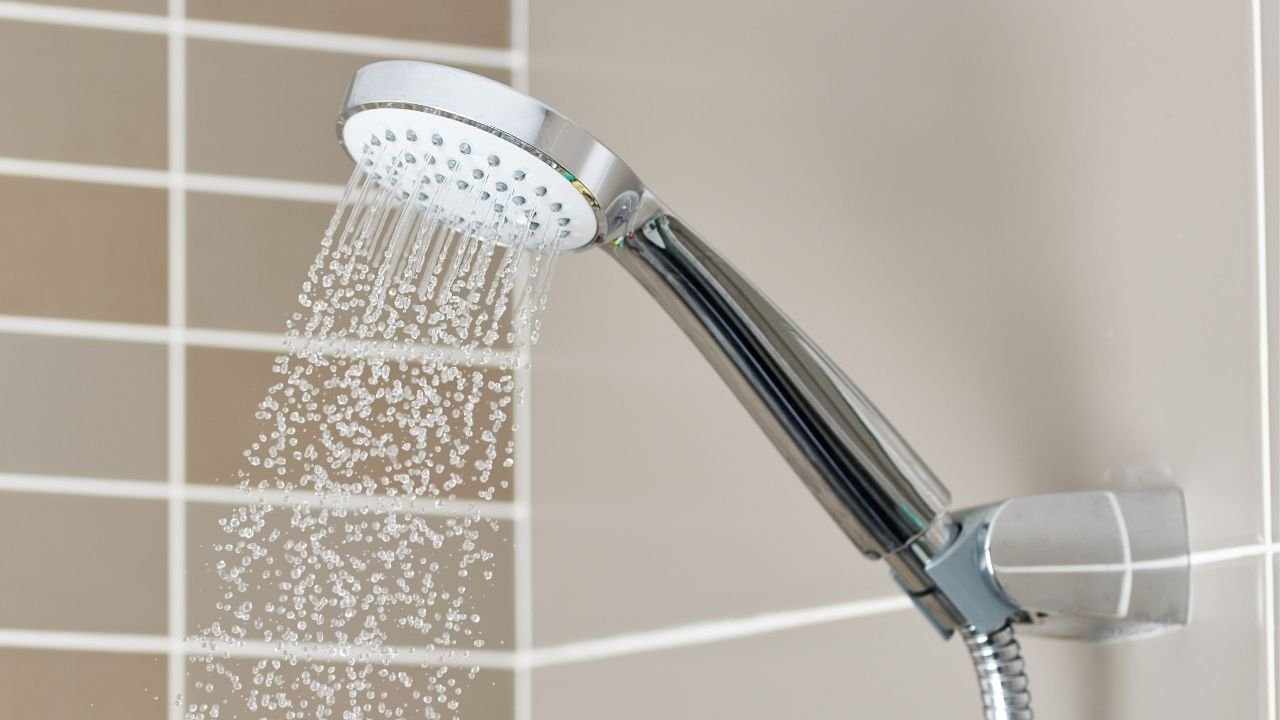 chuveiro moderno com água saindo, instalado em parede de azulejos bege.