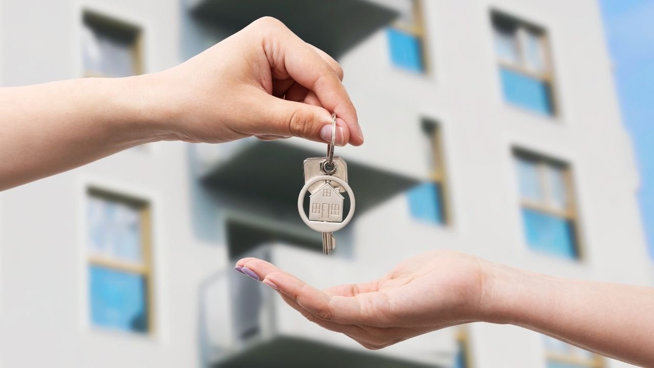 Mãos entregando uma chave com um chaveiro de casa, simbolizando a conclusão da compra de um apartamento.