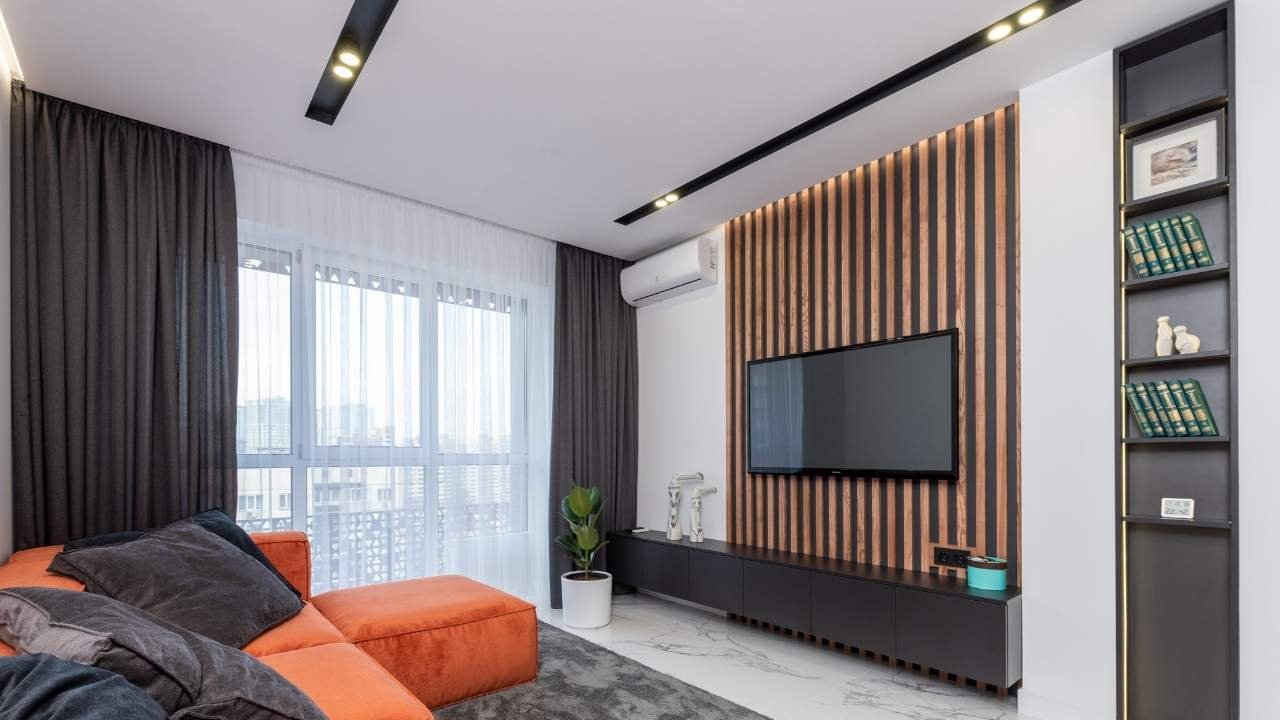 Sala de TV com um painel ripado de madeira escura com iluminação embutida, uma TV e um rack preto, mostrando um exemplo sofisticado de painel para sala de tv.