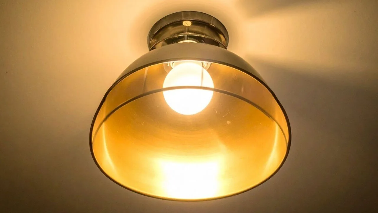 Um dos tipos de luminária de teto mais comuns, este plafon de sobrepor possui um design hemisférico em metal com acabamento dourado na parte interna, emitindo uma luz quente e acolhedora contra o teto branco.