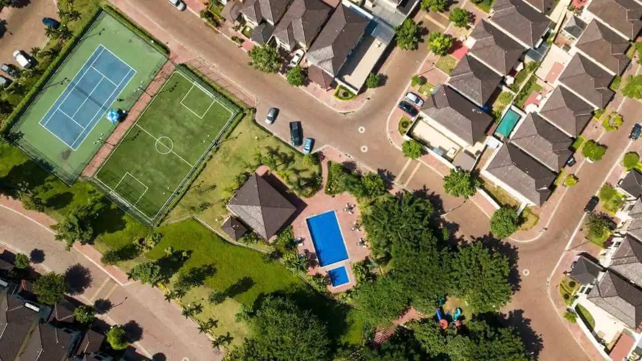 Vista aérea de um condomínio fechado com casas, ruas organizadas, quadras esportivas e piscina.